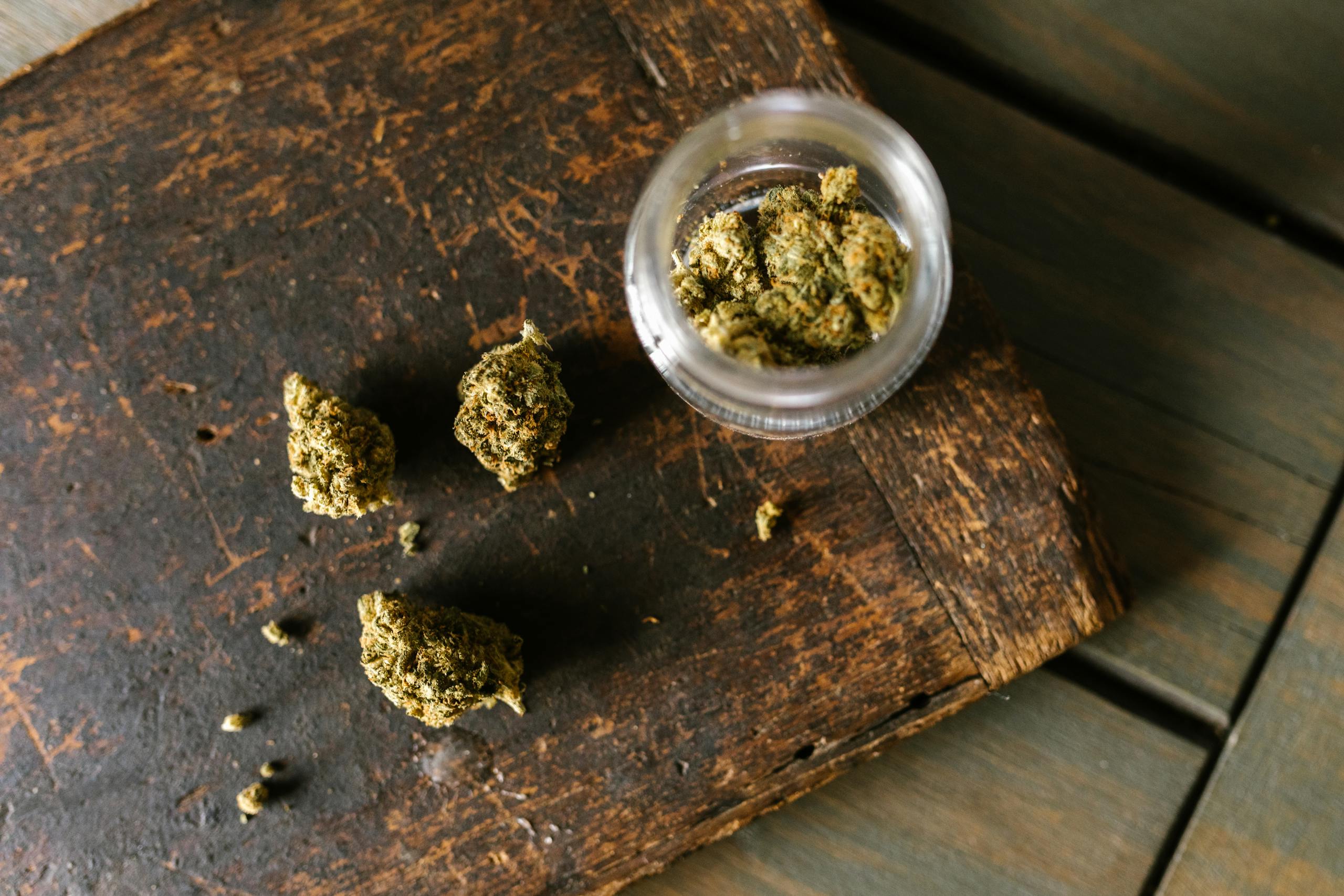 Cannabis buds scattered on a rustic wooden surface with an open jar.