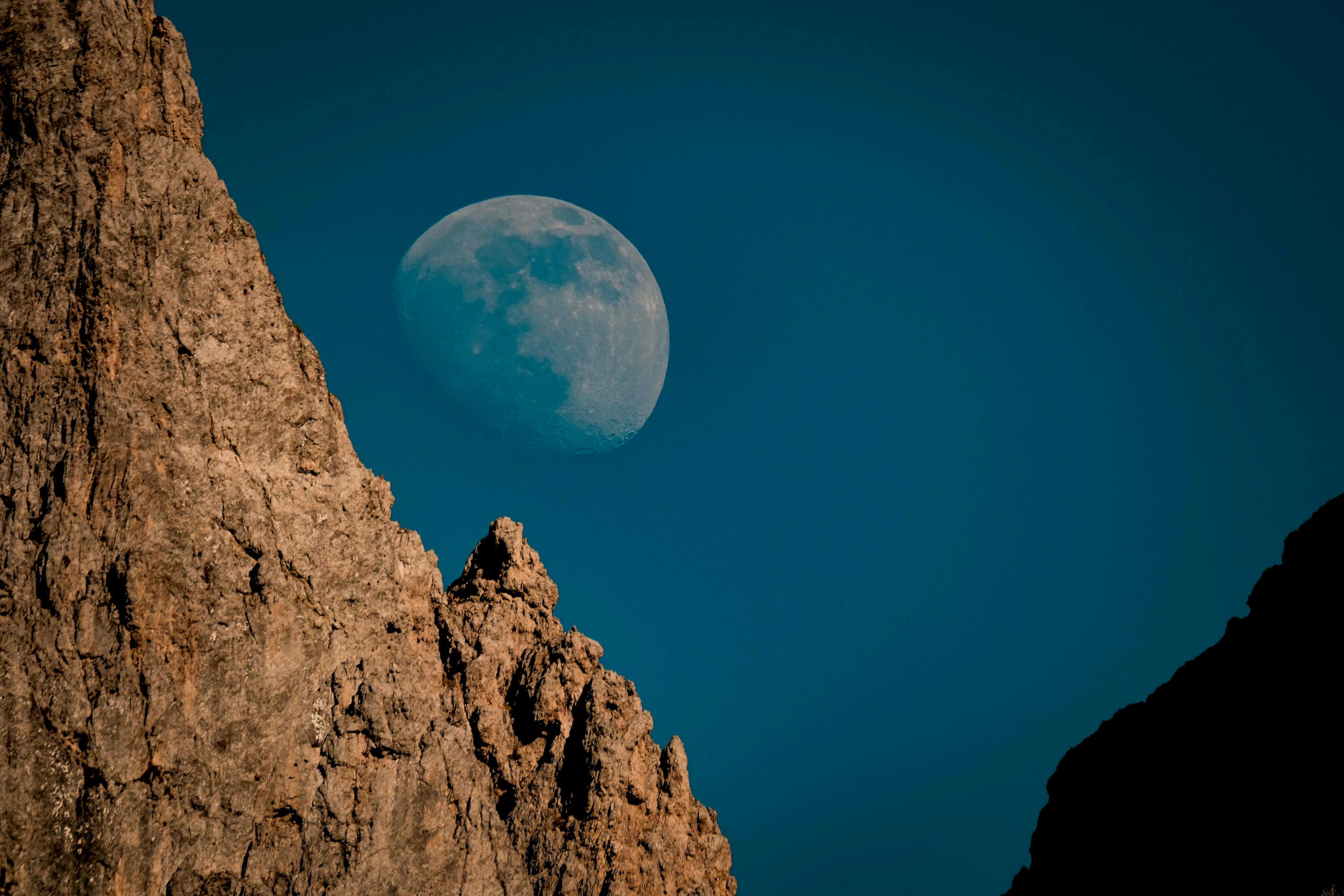 Captivating view of the moon rising over rugged rock formations under a clear sky.
